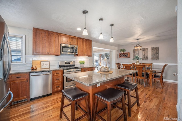 kitchen with a breakfast bar, stainless steel appliances, tasteful backsplash, a kitchen island, and decorative light fixtures