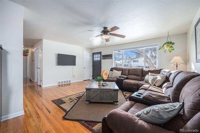 living room featuring ceiling fan, light hardwood / wood-style flooring, and a textured ceiling