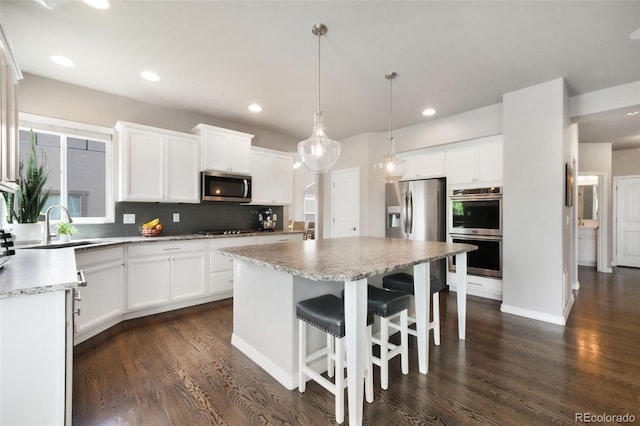 9135 Argentine Pass Trl, Colorado Springs, CO 80924 - kitchen featuring stainless steel appliances, dark wood-type flooring, backsplash, a center island, and white cabinetry