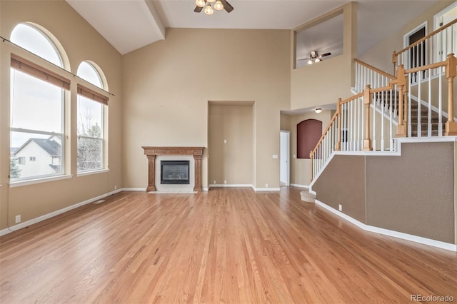 unfurnished living room featuring a glass covered fireplace, baseboards, a ceiling fan, stairs, and wood finished floors