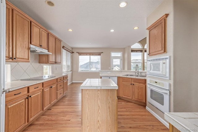 kitchen with white appliances, light wood-style flooring, under cabinet range hood, a sink, and tile counters