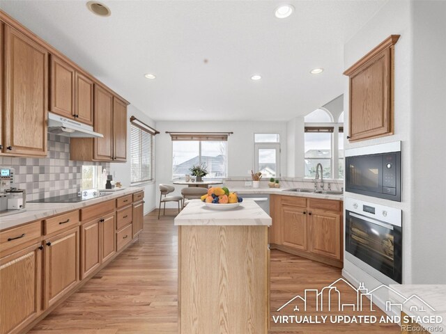 kitchen featuring light wood-style flooring, light countertops, black appliances, under cabinet range hood, and a sink