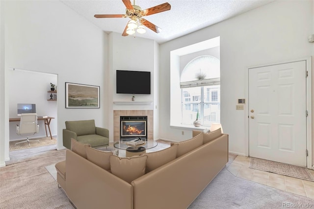 living room with carpet floors, a tiled fireplace, a ceiling fan, a desk, and a textured ceiling
