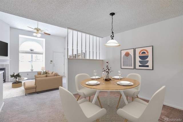 carpeted dining area with ceiling fan, a textured ceiling, a tiled fireplace, and baseboards