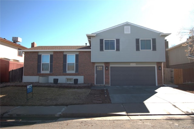 tri-level home featuring a garage, fence, concrete driveway, and brick siding