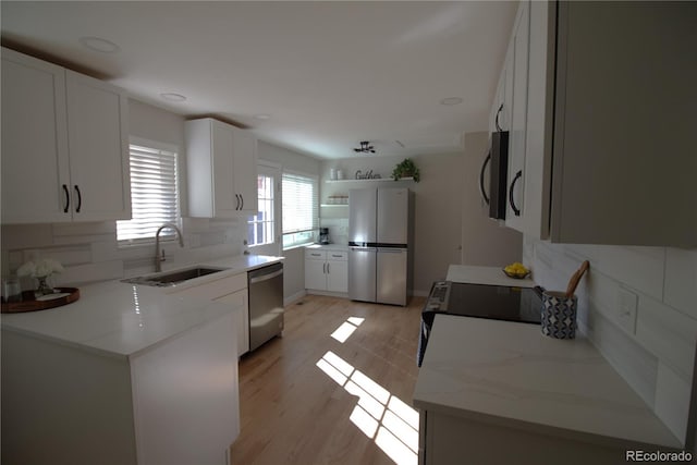 kitchen with light wood-style flooring, stainless steel appliances, a sink, white cabinetry, and decorative backsplash