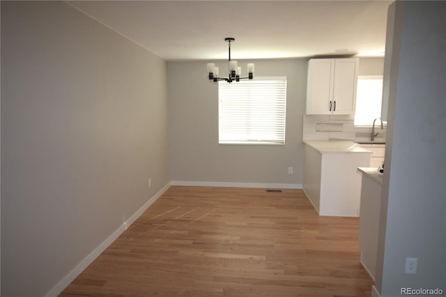 unfurnished dining area featuring light wood-type flooring, an inviting chandelier, a sink, and a healthy amount of sunlight