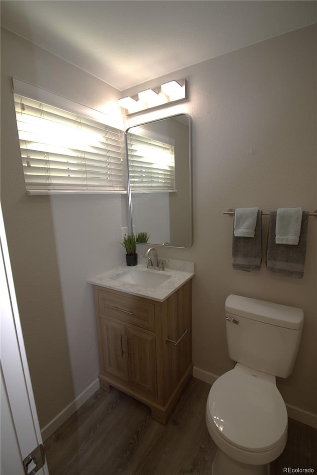 half bath featuring vanity, wood finished floors, toilet, and baseboards