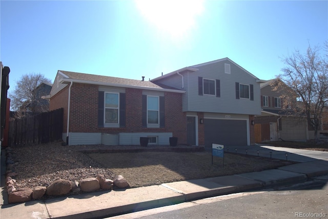 split level home featuring concrete driveway, brick siding, fence, and an attached garage