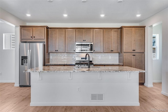 kitchen featuring a breakfast bar area, visible vents, appliances with stainless steel finishes, light stone countertops, and an island with sink