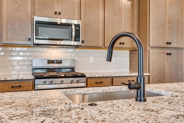 kitchen featuring a sink, light stone counters, stainless steel appliances, and backsplash