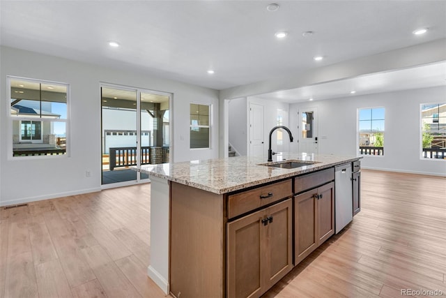 kitchen featuring an island with sink, light wood-style floors, a sink, and light stone countertops