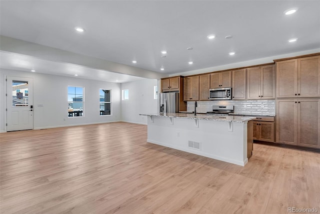 kitchen with a breakfast bar area, visible vents, appliances with stainless steel finishes, light wood-type flooring, and a center island with sink