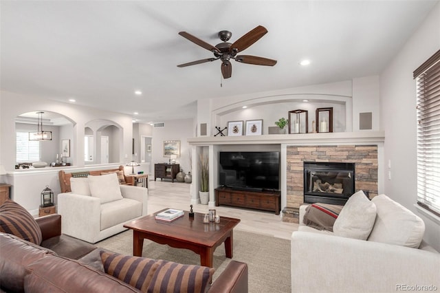 living area featuring visible vents, recessed lighting, ceiling fan, arched walkways, and a stone fireplace
