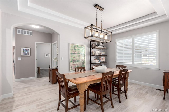 dining area with arched walkways, a raised ceiling, light wood-style floors, and visible vents