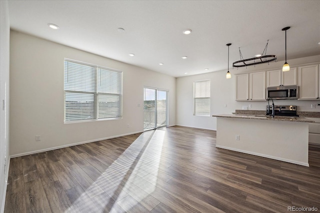 kitchen featuring dark wood-style floors, a kitchen island with sink, hanging light fixtures, appliances with stainless steel finishes, and open floor plan