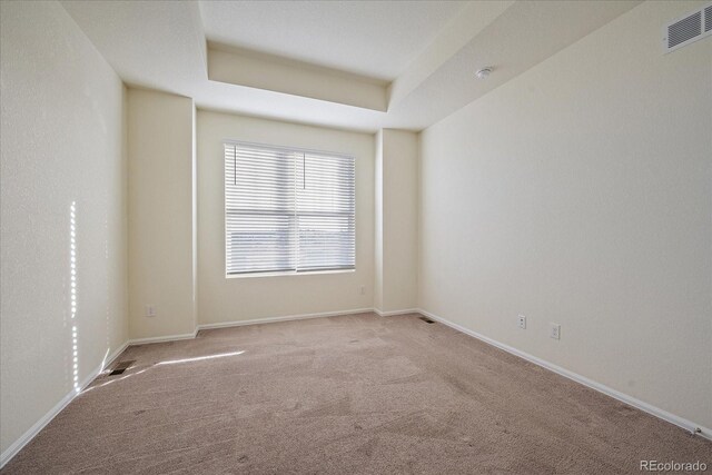 spare room featuring a tray ceiling, carpet flooring, baseboards, and visible vents