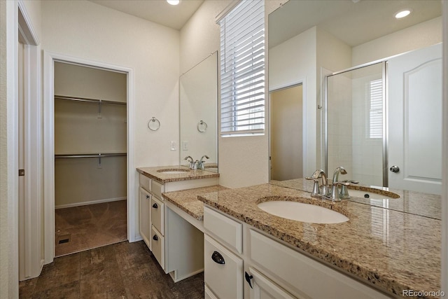 full bath featuring a shower stall, a spacious closet, two vanities, and a sink