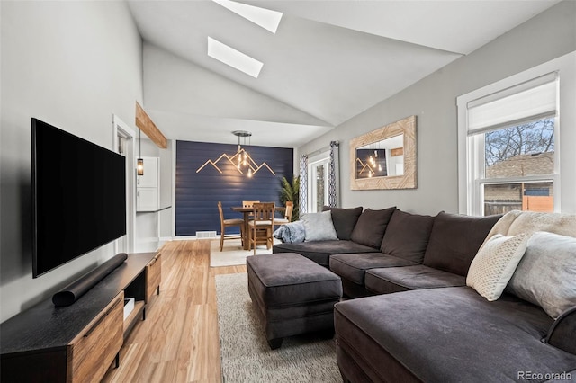 living room with an accent wall, visible vents, lofted ceiling with skylight, and wood finished floors