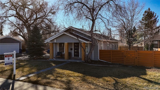 bungalow-style home with a garage, fence, a front lawn, and an outbuilding