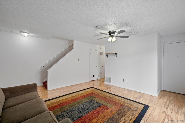 living room featuring visible vents, a ceiling fan, wood finished floors, stairs, and a textured ceiling