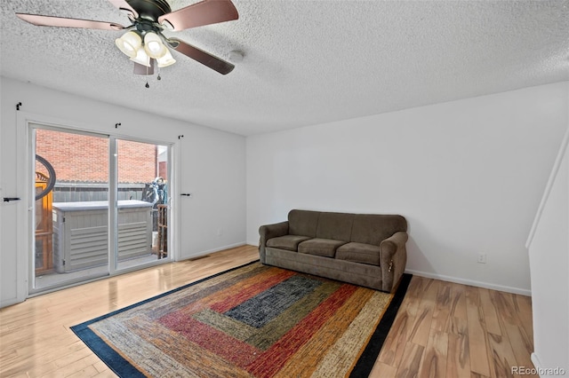 living area featuring light wood-style floors, a textured ceiling, baseboards, and a ceiling fan