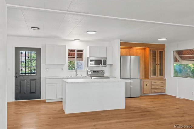 kitchen with sink, light hardwood / wood-style flooring, a kitchen island, white cabinetry, and stainless steel appliances