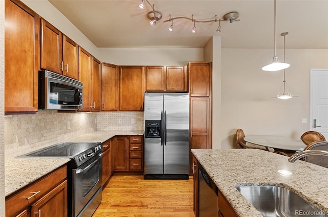 kitchen with light wood finished floors, decorative backsplash, brown cabinets, stainless steel appliances, and a sink