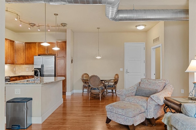 kitchen with visible vents, light wood-type flooring, brown cabinets, stainless steel fridge, and open floor plan