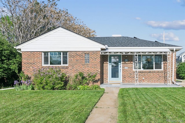 rear view of house featuring a lawn, brick siding, a porch, and roof with shingles