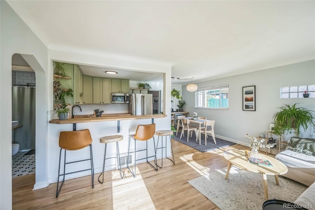 kitchen featuring stainless steel appliances, green cabinetry, butcher block countertops, a breakfast bar area, and light wood-type flooring