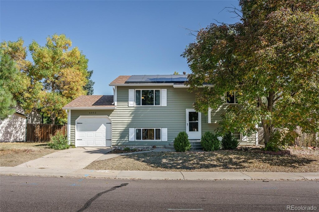 split foyer home featuring an attached garage, fence, solar panels, and driveway