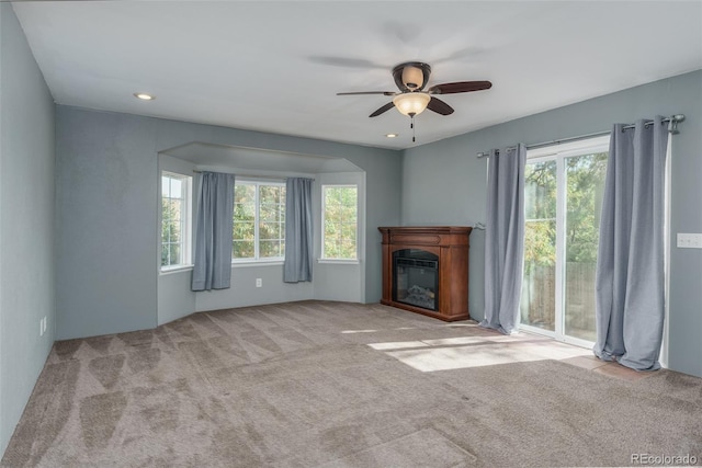 unfurnished living room featuring a healthy amount of sunlight, ceiling fan, and light carpet