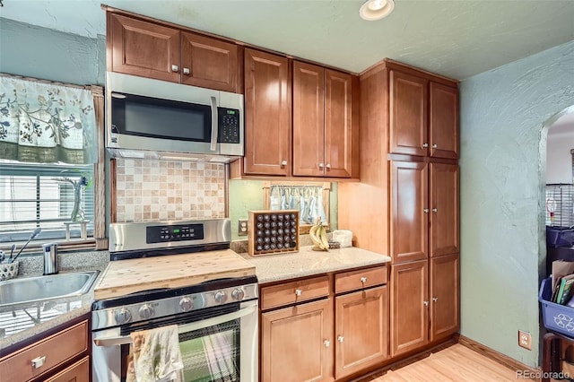 5704 Ammons St, Arvada, CO 80002 - kitchen featuring stainless steel appliances, light wood-style flooring, a sink, arched walkways, and brown cabinetry