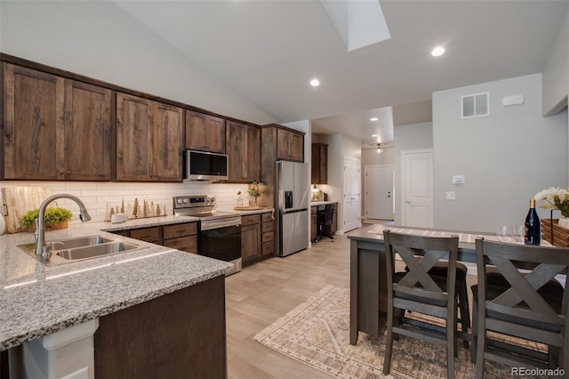 kitchen with dark brown cabinets, stainless steel appliances, tasteful backsplash, sink, and light wood-type flooring