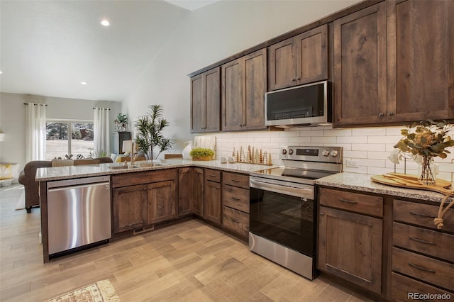 kitchen featuring kitchen peninsula, dark brown cabinets, stainless steel appliances, light stone counters, and tasteful backsplash