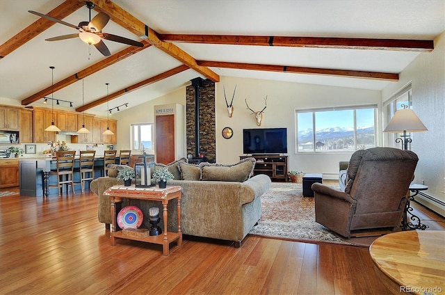 living area with ceiling fan, hardwood / wood-style floors, lofted ceiling with beams, and a wood stove