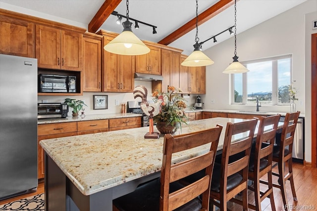 kitchen with under cabinet range hood, stainless steel appliances, wood finished floors, a sink, and brown cabinetry