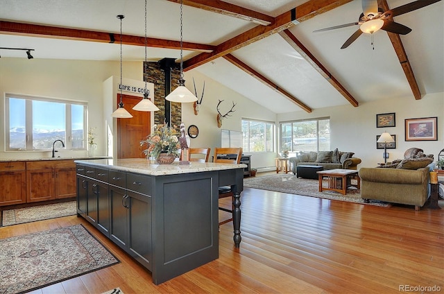 kitchen featuring a breakfast bar area, light wood-style floors, open floor plan, beam ceiling, and light stone countertops