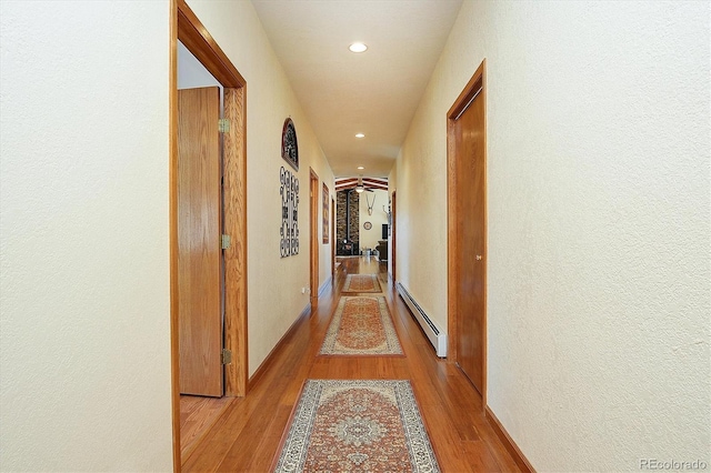 hallway featuring a baseboard heating unit, wood finished floors, and recessed lighting