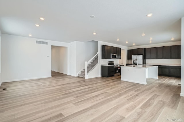 kitchen with dark brown cabinetry, stainless steel appliances, a kitchen island with sink, and light wood-type flooring