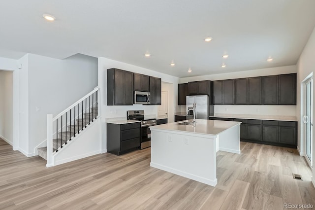 kitchen featuring stainless steel appliances, an island with sink, sink, and light hardwood / wood-style floors