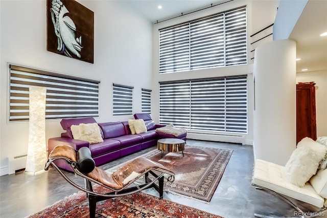 living room with concrete flooring, a baseboard heating unit, and a towering ceiling