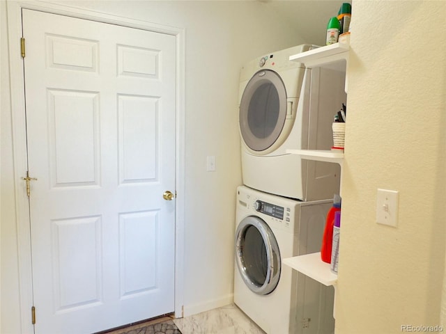 clothes washing area featuring marble finish floor, stacked washer and dryer, and laundry area