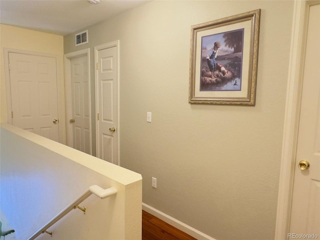 corridor with an upstairs landing, dark wood-type flooring, baseboards, and visible vents