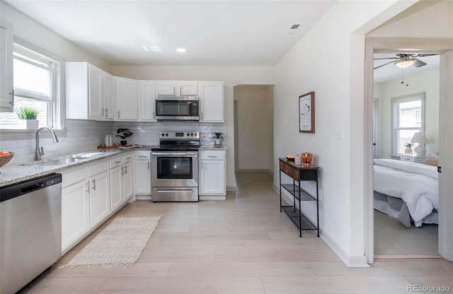 kitchen featuring a ceiling fan, backsplash, appliances with stainless steel finishes, light stone countertops, and a sink
