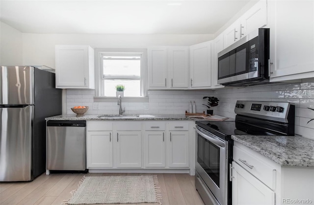kitchen with light wood-style floors, a sink, decorative backsplash, and appliances with stainless steel finishes