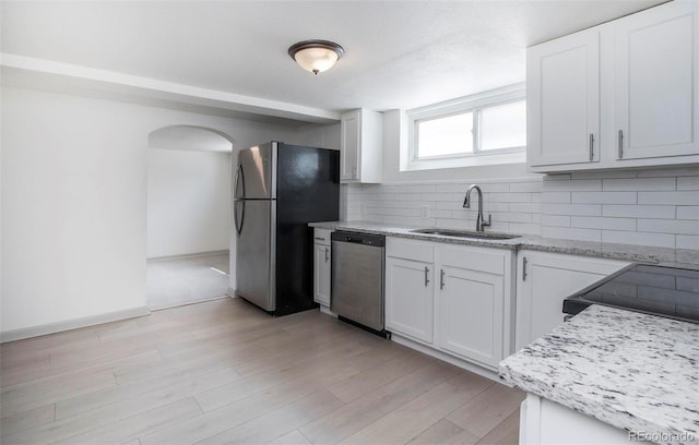 kitchen featuring backsplash, light wood-type flooring, a sink, white cabinets, and stainless steel appliances