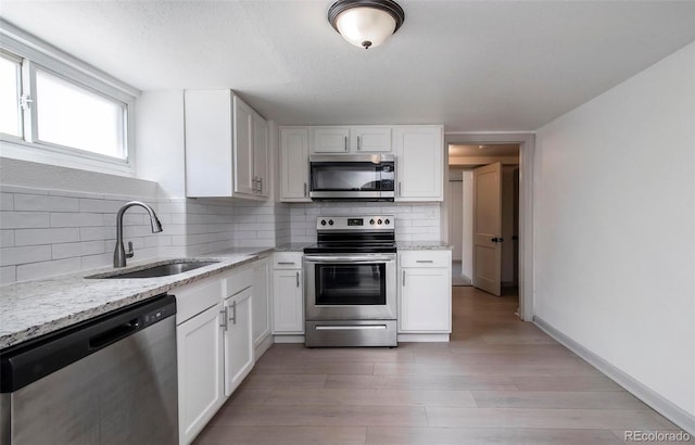 kitchen with a sink, light stone counters, stainless steel appliances, and white cabinetry