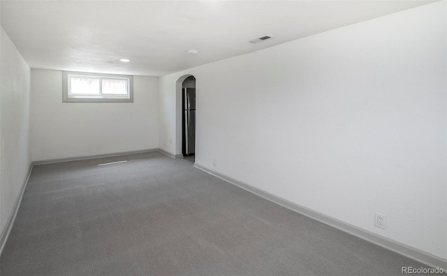 carpeted spare room with visible vents, arched walkways, and baseboards